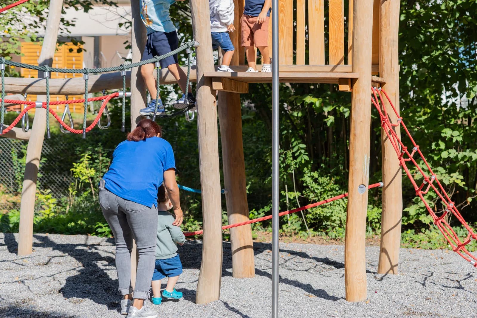 Betreuerin begleitet Kleinkind am Kletterturm auf dem Spielplatz